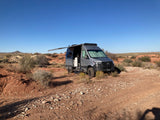 Gray Sprinter van RV rental set up for remote desert camping with awning extended.