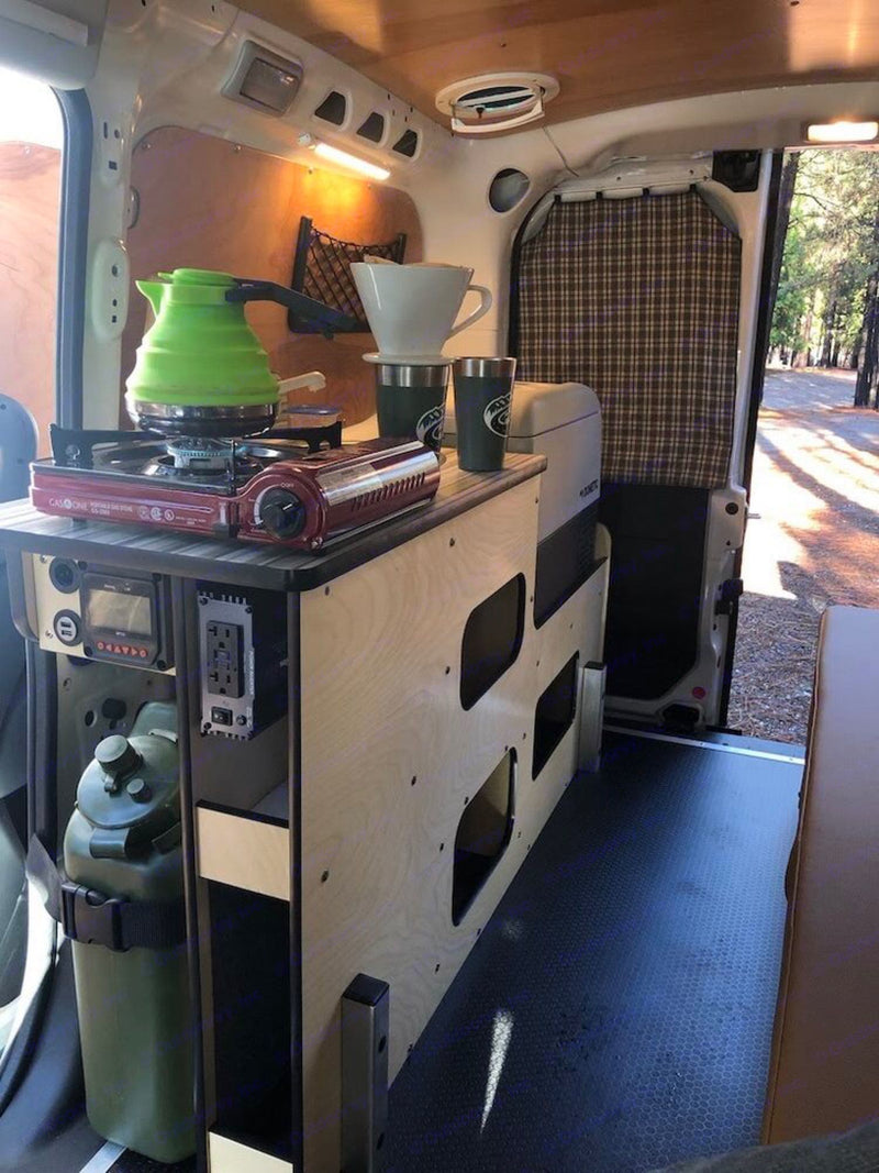  all within wood-paneled walls.|White RV rental camper van with glowing interior lights under a brilliant starry night sky with distant mountains.|RV rental's power setup: a blue solar charge controller and an orange/black 400W inverter offer USB/AC outlets.|Inside an rv rental: a cozy camper van kitchen with portable stove — photo 6