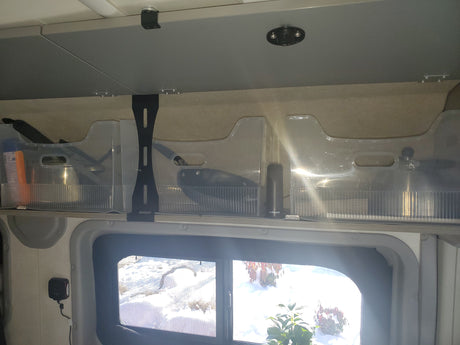 RV rental interior showing organized overhead storage with clear bins, kitchenware, a weBoost, and snowy outdoor view.