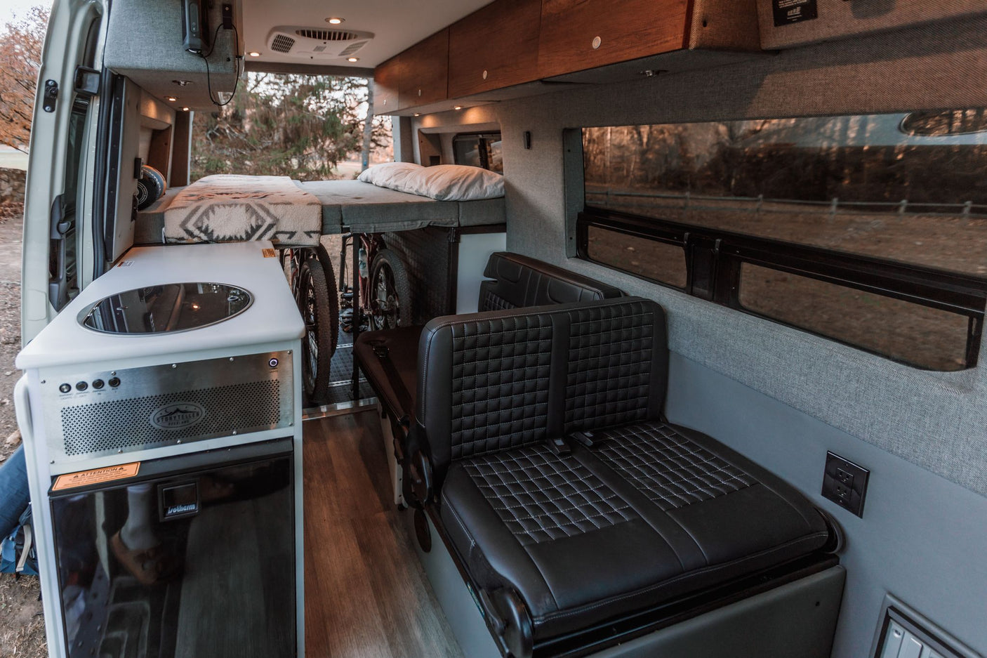 Modern RV rental interior with kitchen, elevated bed, passenger seating, & secure bike storage. Explore in comfort.