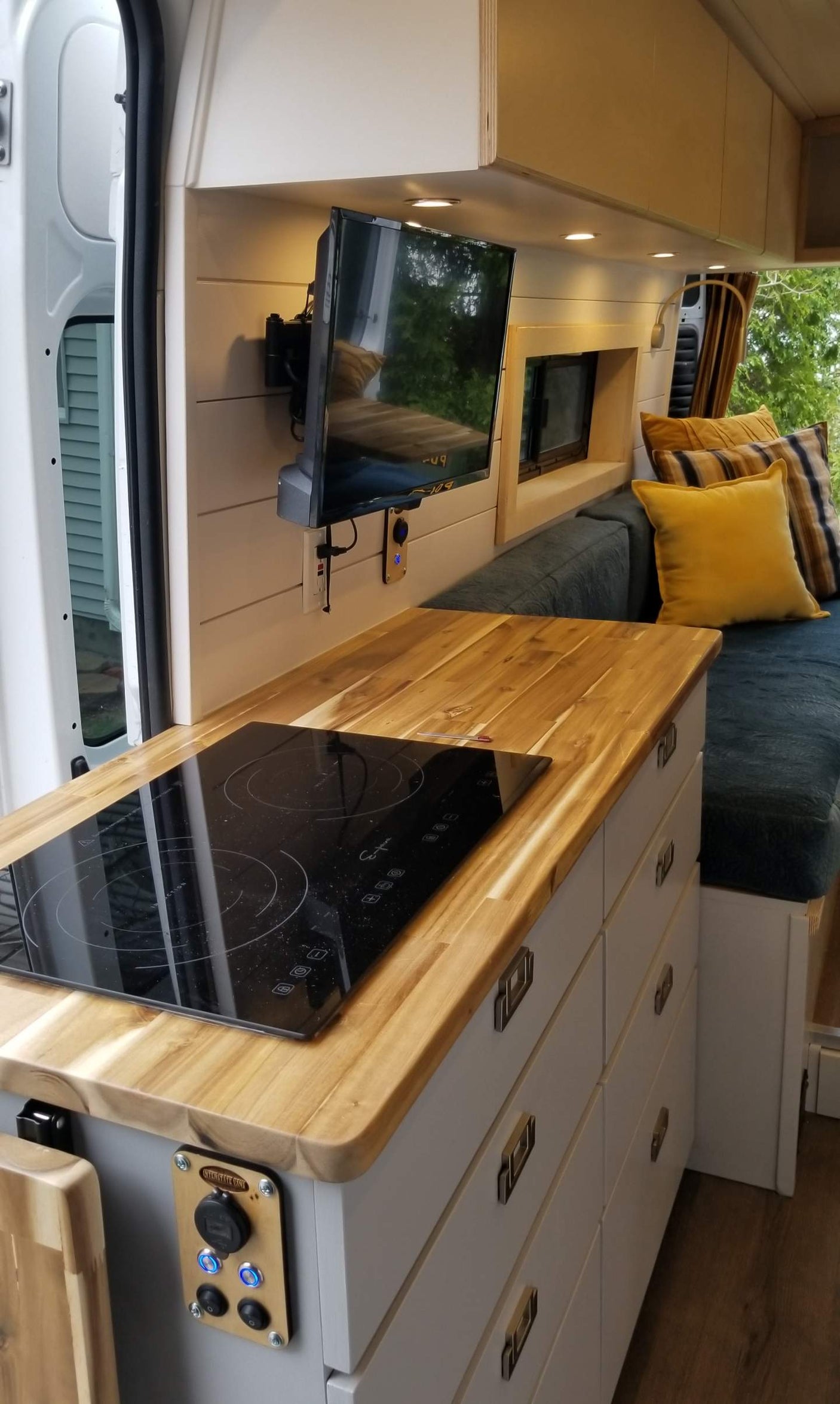 View inside a modern rv rental showing a sleek kitchen with induction cooktop, wall-mounted TV, and cozy bench. Ideal for van life.