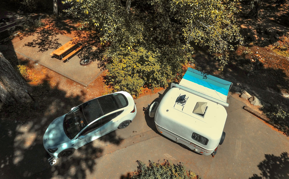Overhead view of a Tesla and a Scamp RV rental parked at a serene campsite with picnic amenities. — photo 19