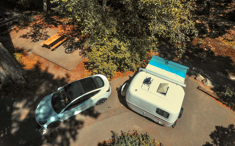 Overhead view of a Tesla and a Scamp RV rental parked at a serene campsite with picnic amenities. — photo 19