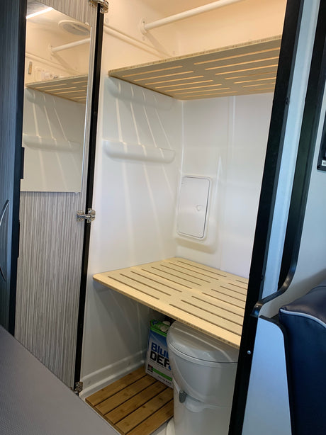This RV rental features a functional, compact interior with a toilet, tiered slatted shelves, and a wooden floor mat.