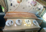 Cozy RV rental interior: kitchen with sink, countertop, and dining area with plates & cutlery, adorned with decorative wall art.