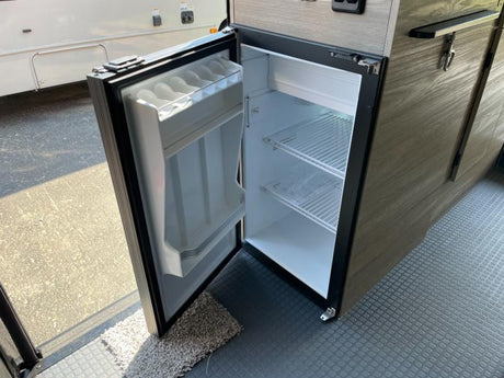 An RV rental's compact refrigerator is open, revealing its interior wire shelves and door storage, part of a functional camper kitchen.