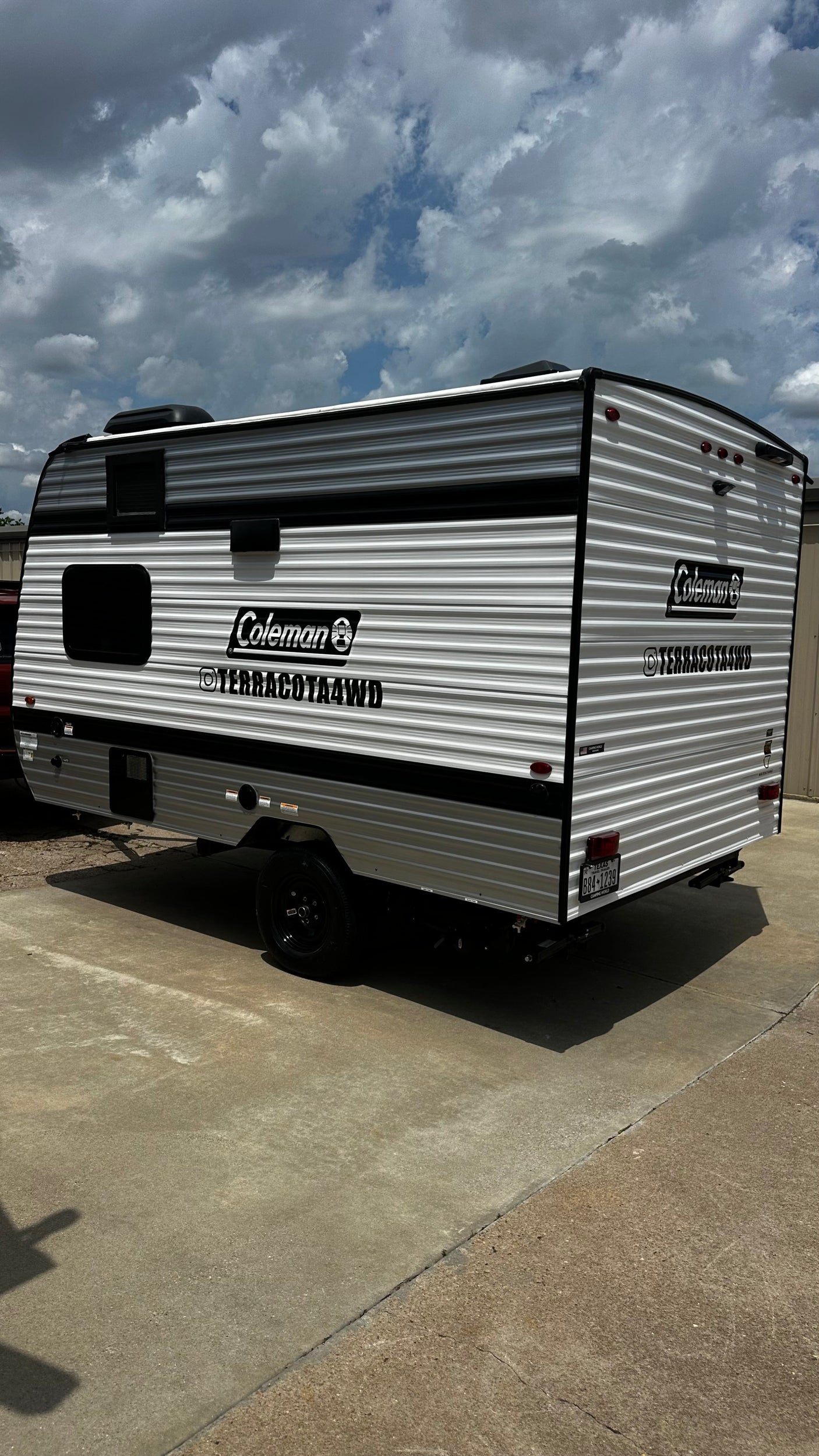 New Coleman Terracota4WD travel trailer for rv rental. Sleek white and black camper on concrete under a cloudy sky.