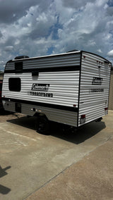 New Coleman Terracota4WD travel trailer for rv rental. Sleek white and black camper on concrete under a cloudy sky.