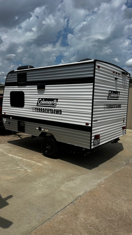 New Coleman Terracota4WD travel trailer for rv rental. Sleek white and black camper on concrete under a cloudy sky.