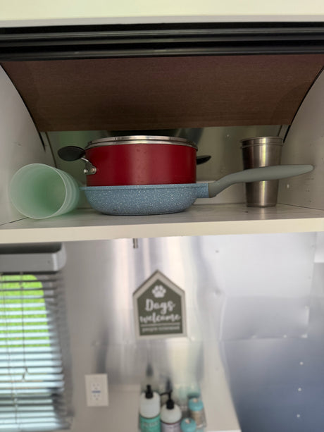 An rv rental kitchen with a red pot, blue pan, and cups neatly stored on a shelf. Ready for compact adventures.