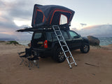 Sunset over an SUV with a rooftop tent and chairs on a sandy beach by the ocean. Ideal for an RV rental adventure.