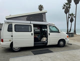 White pop-top camper van (RV rental) at the beach, side door open. Perfect for oceanfront relaxation.