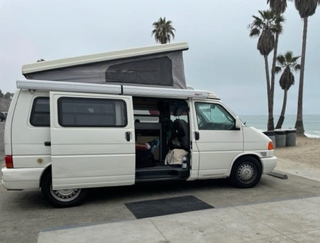 White pop-top camper van (RV rental) at the beach, side door open. Perfect for oceanfront relaxation.