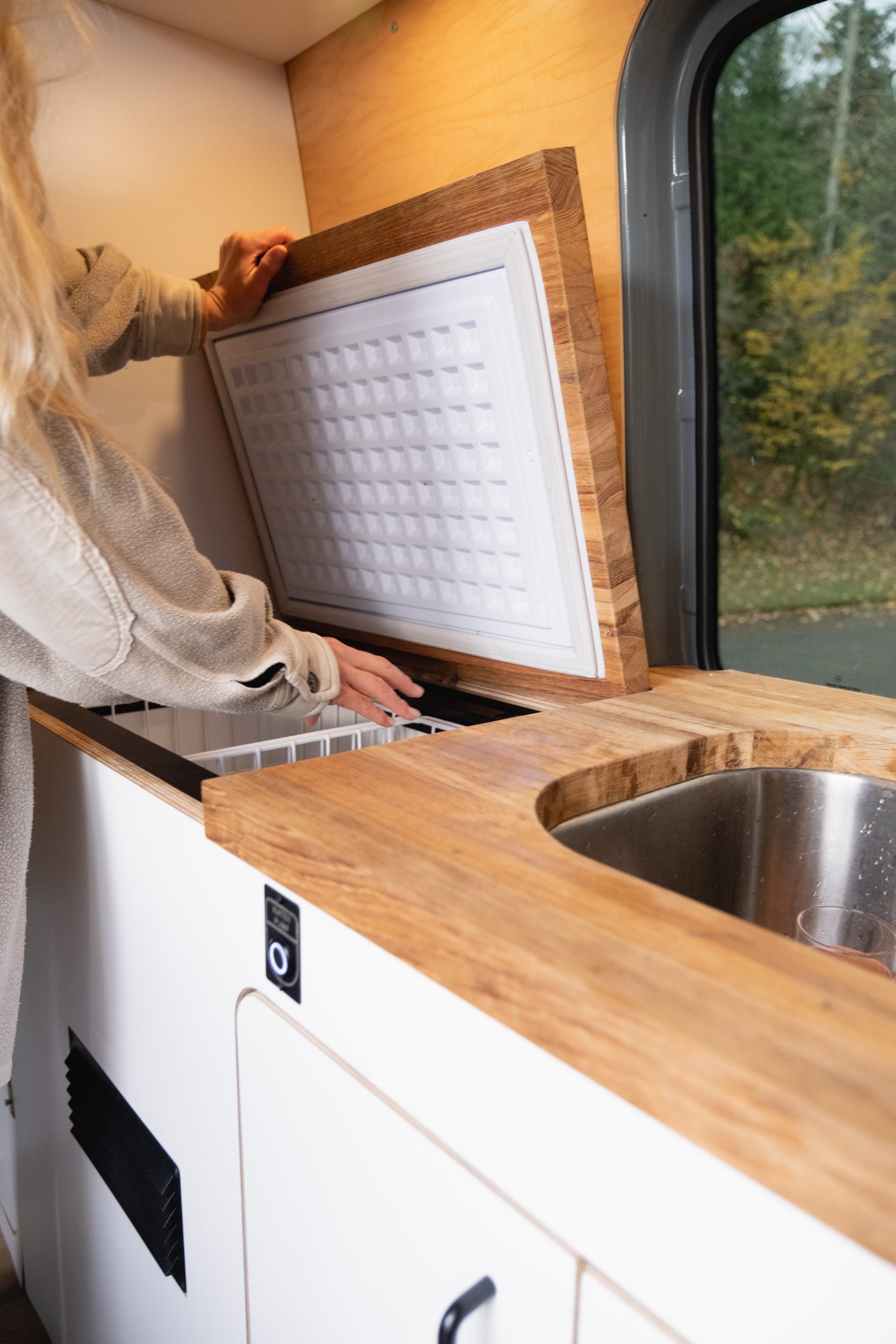 RV rental: person opens built-in fridge in modern kitchen with wood counter, sink.