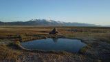 RV rental: A truck with a pop-up tent camps by a tranquil hot spring, reflecting snowy mountains and vast plains.