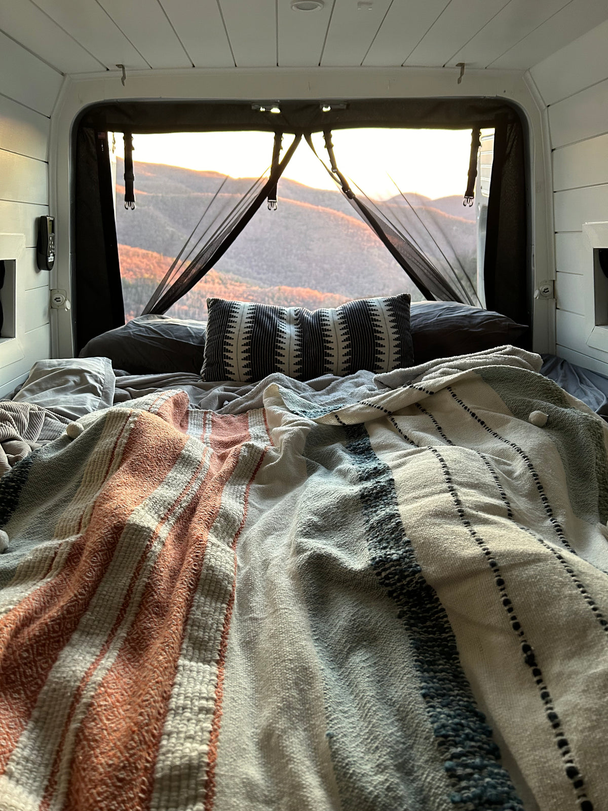Cozy **rv rental** bed with mountain sunset views through a mesh screen, ideal for van life adventures. — photo 7