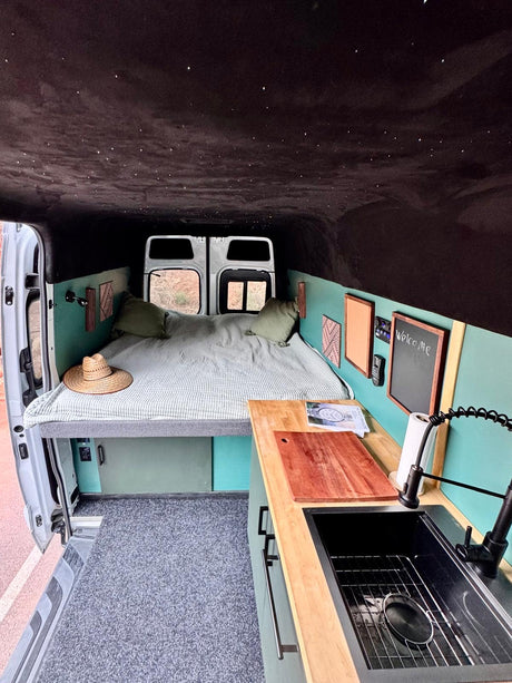 Cozy RV rental interior: starry ceiling, comfy bed, and functional kitchen in a charming camper van setup.