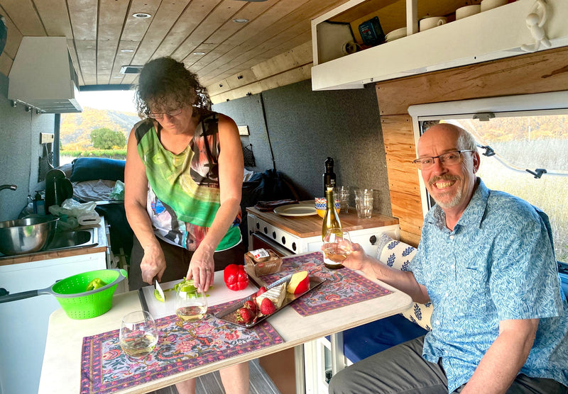 Inside a roomy RV rental, a couple cooks and dines, enjoying wine and picturesque views from their comfortable travel space. — photo 11