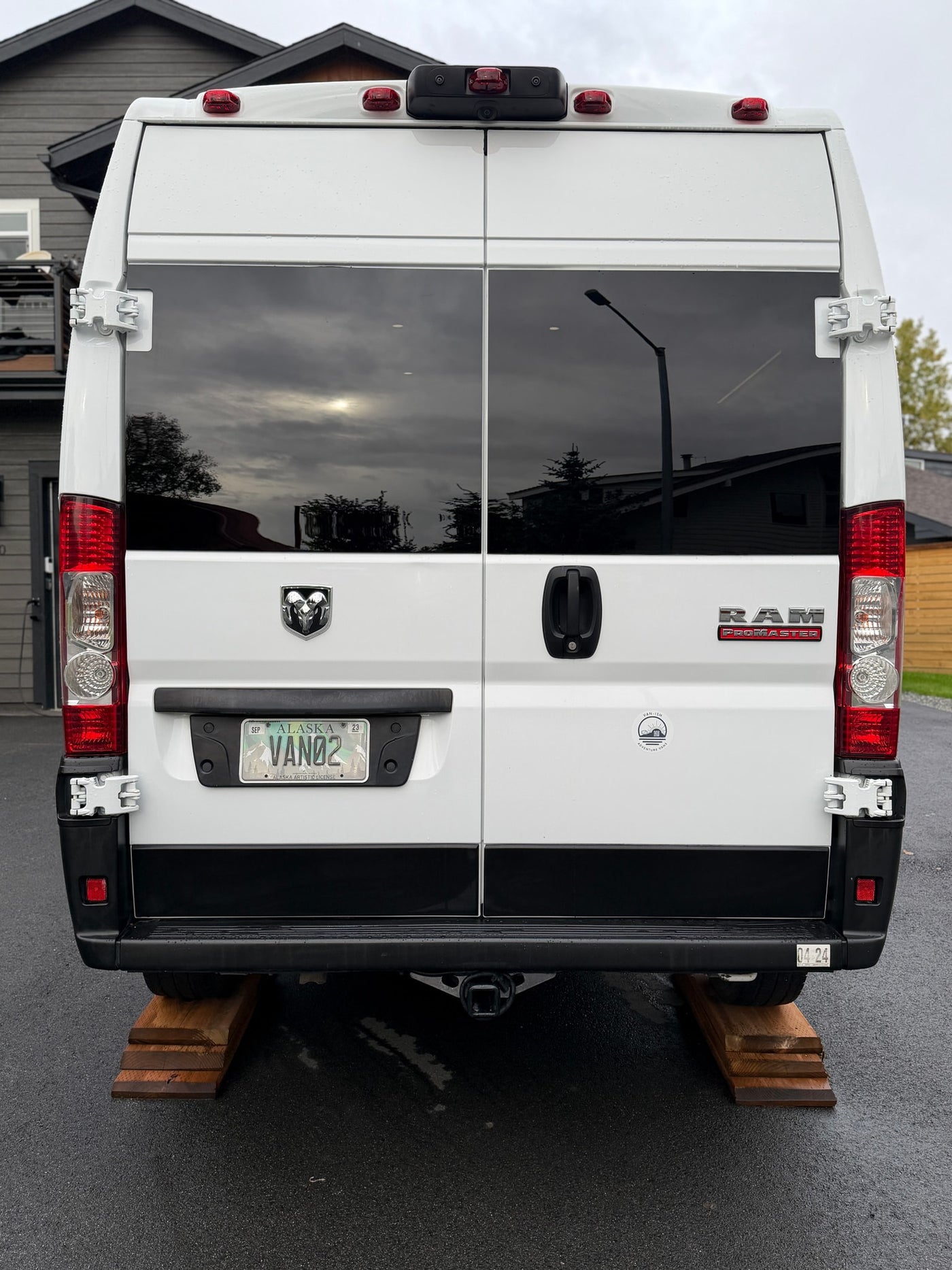 Rear view of a white Ram ProMaster rv rental van, identified by its Alaska "VAN02" plate, parked on wooden leveling blocks. — photo 7