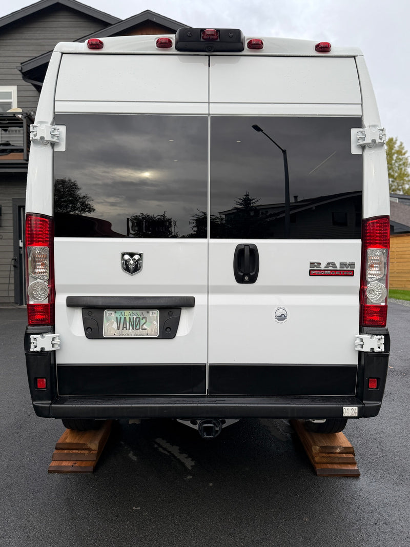 Rear view of a white Ram ProMaster rv rental van, identified by its Alaska "VAN02" plate, parked on wooden leveling blocks. — photo 7