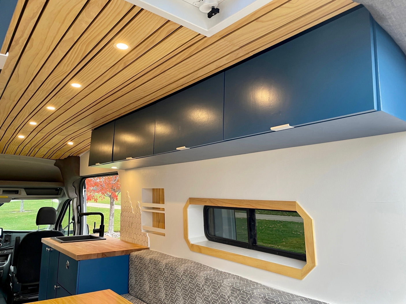 Spacious camper van interior, ideal for an rv rental. Features modern blue cabinets, wood ceiling, kitchen, and window.