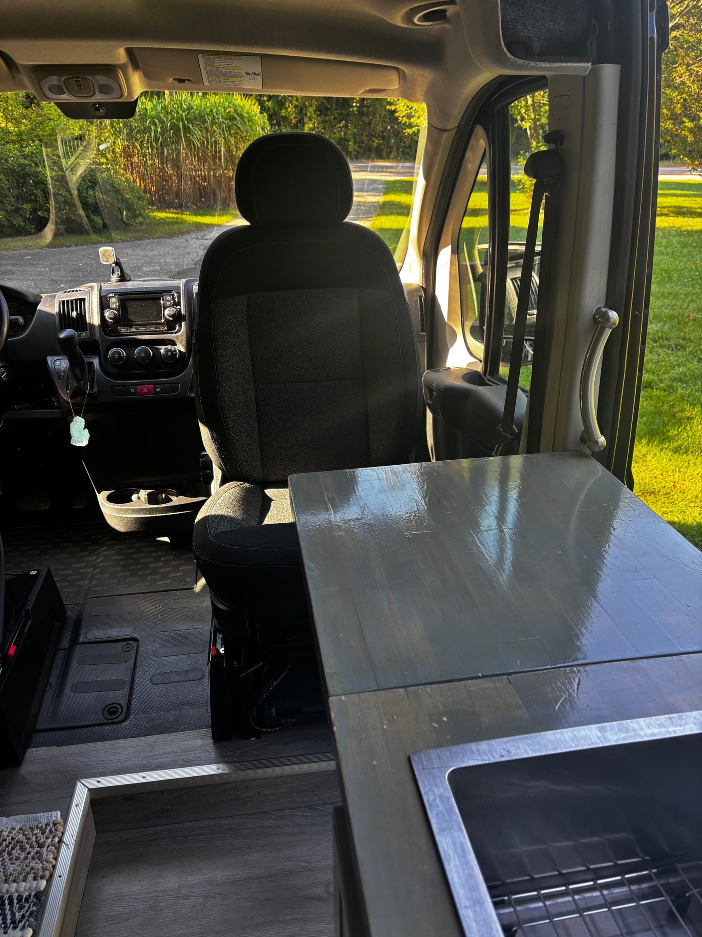 View inside an rv rental camper van: driver's seat, dashboard, and kitchen counter with sink. Green outdoors.