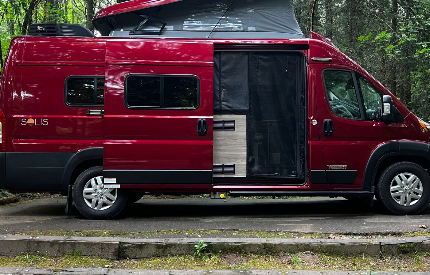  perfect for travel.|A red Winnebago Solis RV rental is parked in a serene forest campground — photo 5