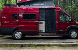 A bright red Winnebago Solis campervan, perfect for an RV rental, showcasing its open side door in a forest.