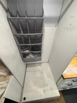 Compact RV rental interior featuring a gray multi-pocket hanging organizer, white walls, and a wooden kitchen counter with cabinets.
