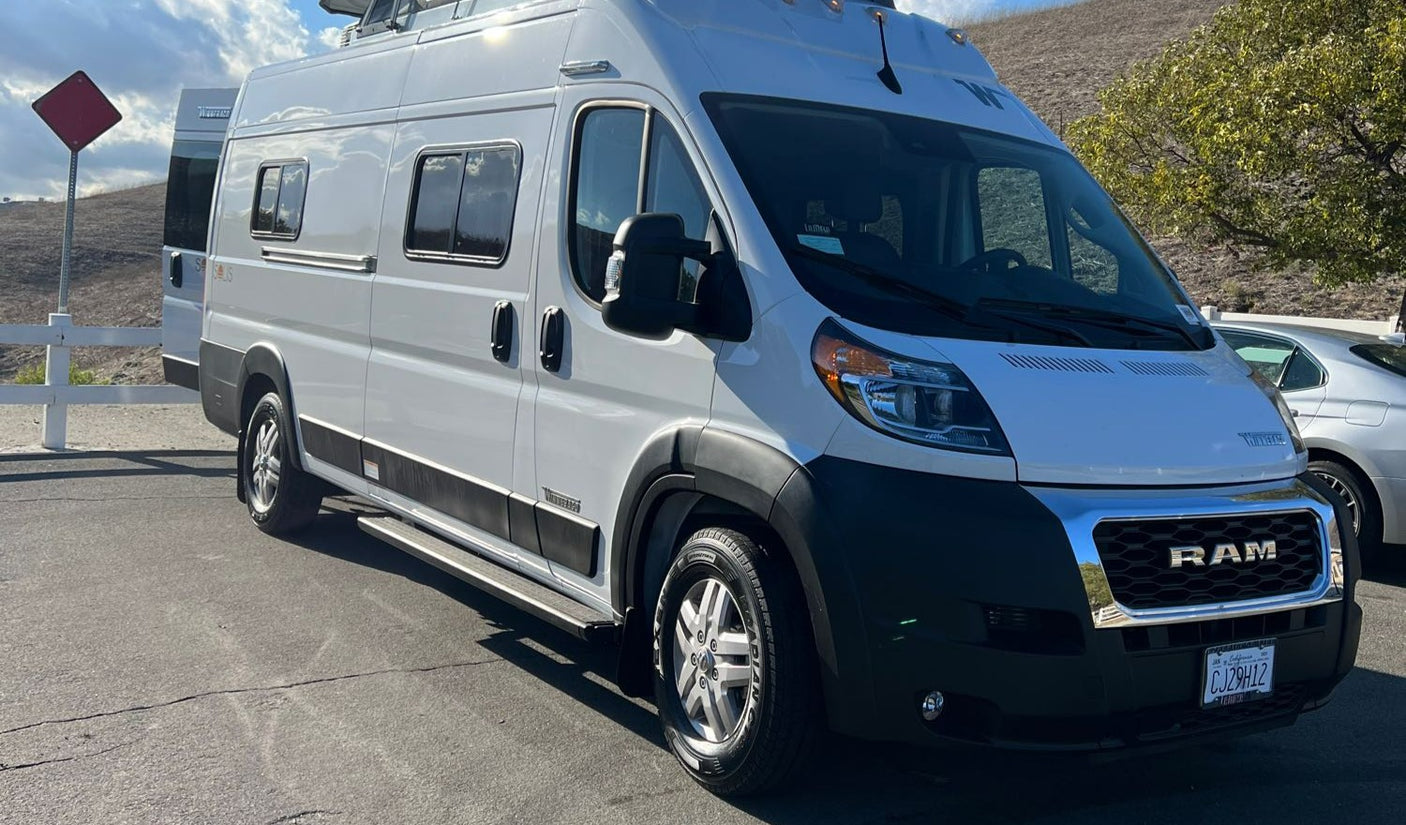 A white Winnebago camper van, built on a Ram ProMaster chassis, ideal for RV rental, parked outdoors on a sunny day.