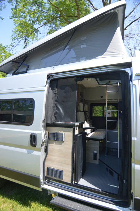 RV rental with open side door revealing a versatile interior: convertible bed, seating, and bunk ladder. Awning extended.