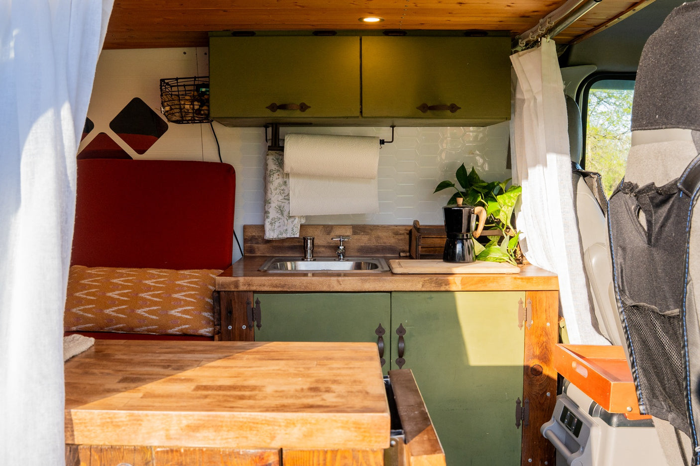 RV rental: Compact custom kitchen & living area with green cabinets, sink, plant, and red seating.