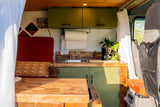 RV rental: Compact custom kitchen & living area with green cabinets, sink, plant, and red seating.