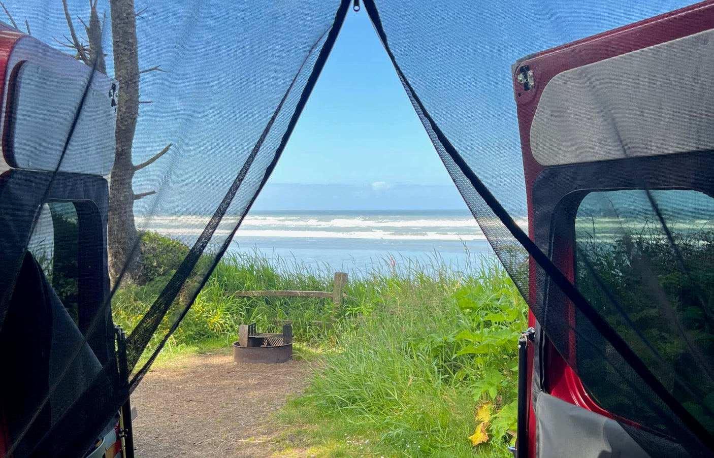 Relaxing inside an RV rental with an amazing ocean view. The camper van's mesh screens frame a beach campsite with a fire pit.