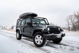 Dark Jeep Wrangler with roof cargo box on a snowy road in Montana. Perfect for rugged winter adventures, similar to an RV rental trip.