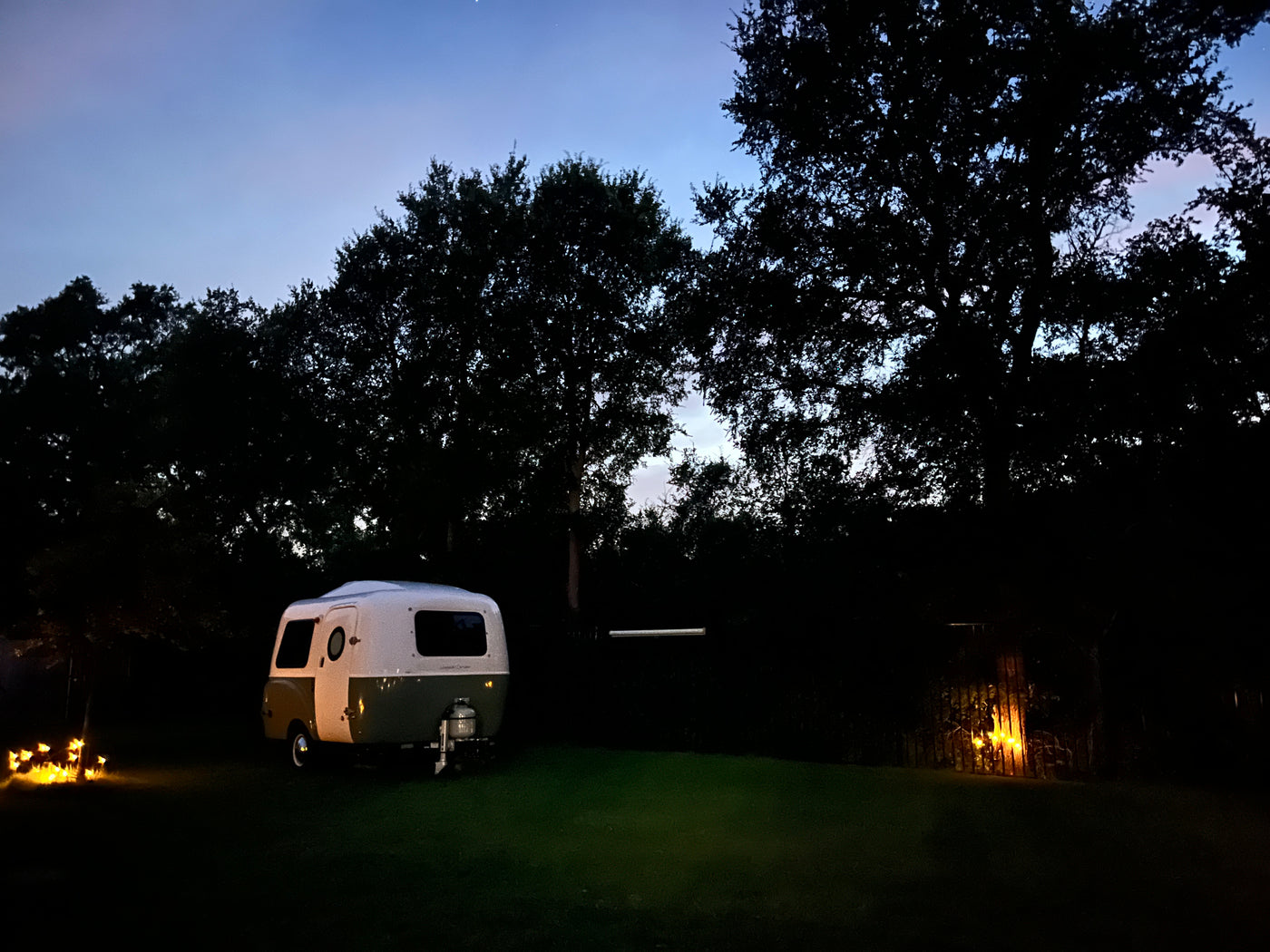 This peaceful evening scene shows a charming white and green RV rental parked on a grassy lawn under a twilight sky with silhouetted trees. — photo 3