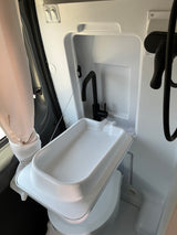 Compact RV rental bathroom with foldable sink, black faucet, and shower setup for efficient space use.