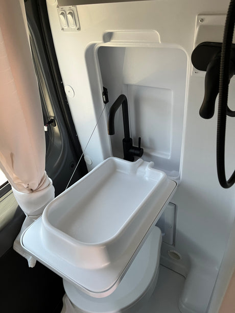 Compact RV rental bathroom with foldable sink, black faucet, and shower setup for efficient space use.