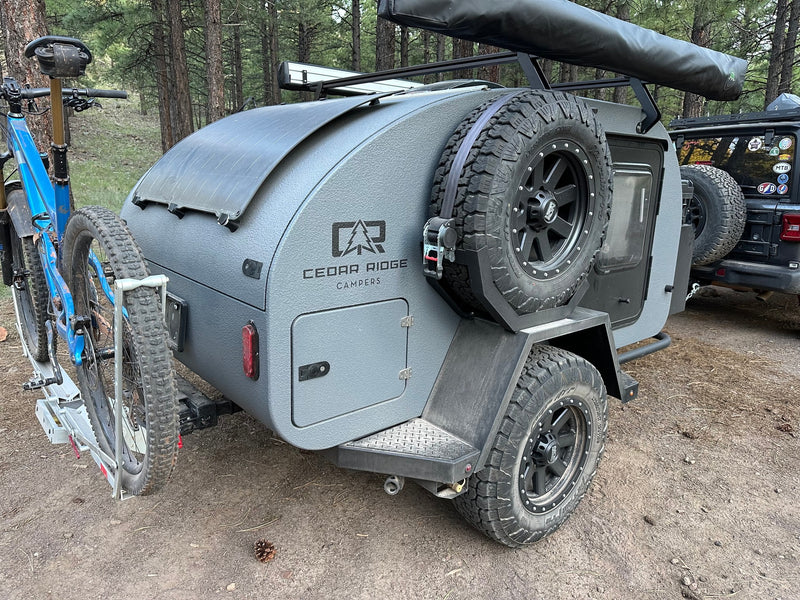 Gray Cedar Ridge teardrop camper RV rental with mountain bike, solar panel, spare tire, and awning ready for forest adventures. — photo 8