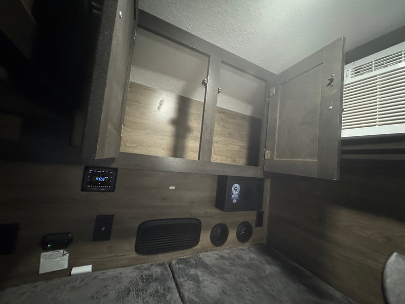 RV rental bedroom area with open storage cabinets, an AC unit, media control panel, and a small safe. — photo 9