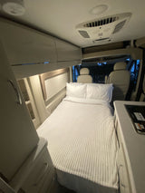 Explore this RV rental: a cozy bed, compact kitchen, and driver's area inside a clean, well-appointed camper van.
