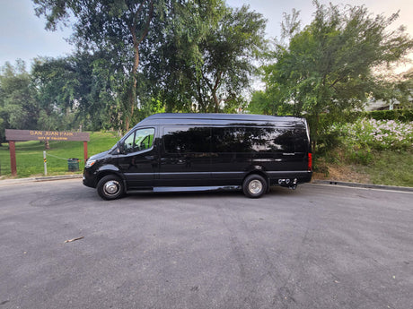 Black Mercedes Sprinter van RV rental parked at San Juan Park, City of Fullerton, with park sign & trees.
