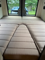Comfortable modular bed in this rv rental, with a view of a car and trees through the rear windows.