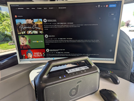 Inside an RV rental, a monitor displays Prime Video movies like Home Alone, alongside an Anker speaker, Xbox controller, and mouse for entertainment.