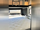 RV rental interior: A comfortable bedroom with a large, white patterned mattress and windows, ready for your next adventure.