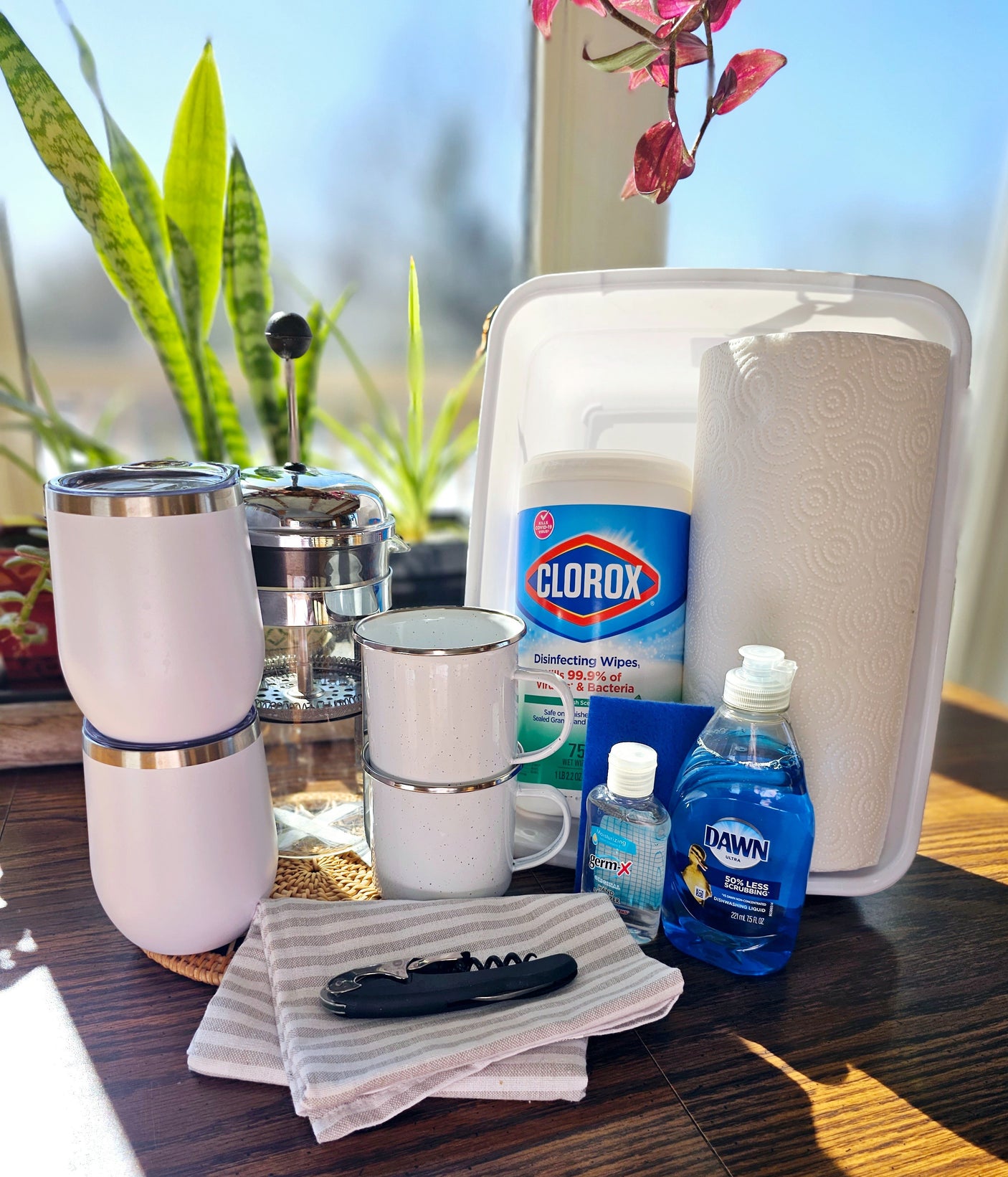 RV rental trip prep: Coffee press, mugs, tumblers, and cleaning essentials like wipes, soap, and sanitizer.
