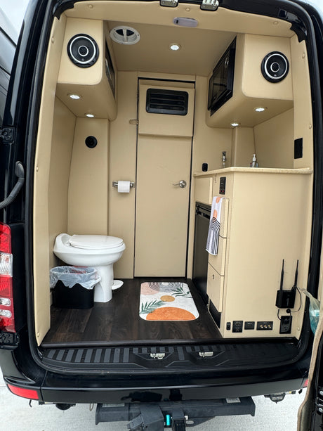 Rear view of an RV rental van conversion, showcasing a compact kitchen, toilet, and well-equipped living space.