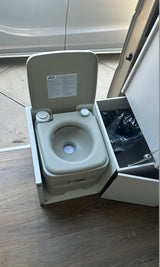 Inside the RV rental: a compact, portable toilet with adjacent storage for convenient mobile travel.