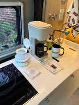 An rv rental's compact kitchen with a Bella coffee maker, folding electric kettle, induction cooktop, and sink area.