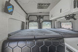 Spacious rv rental van interior: back view of the large bed, black leather bench, white cabinets, & mountain road scenery.